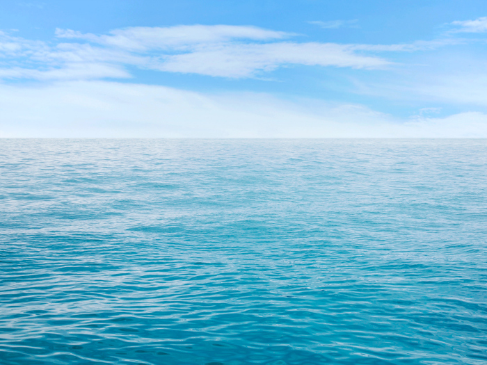 Superficie del océano en un día soleado con cielo despejado y agua azul clara.