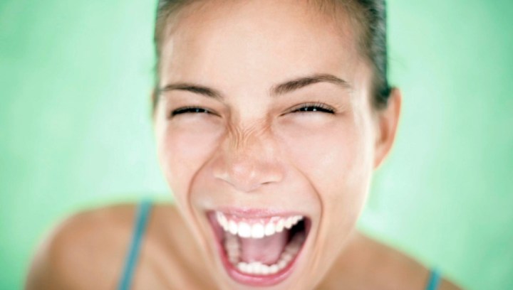Joven sonriendo y riendo con entusiasmo frente a un fondo verde.
